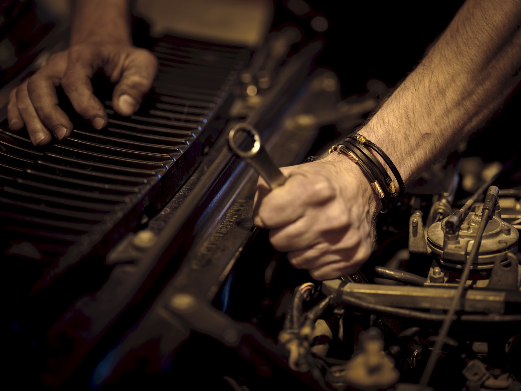 A mechanic's grease-stained hands turning a metal wrench on an engine component