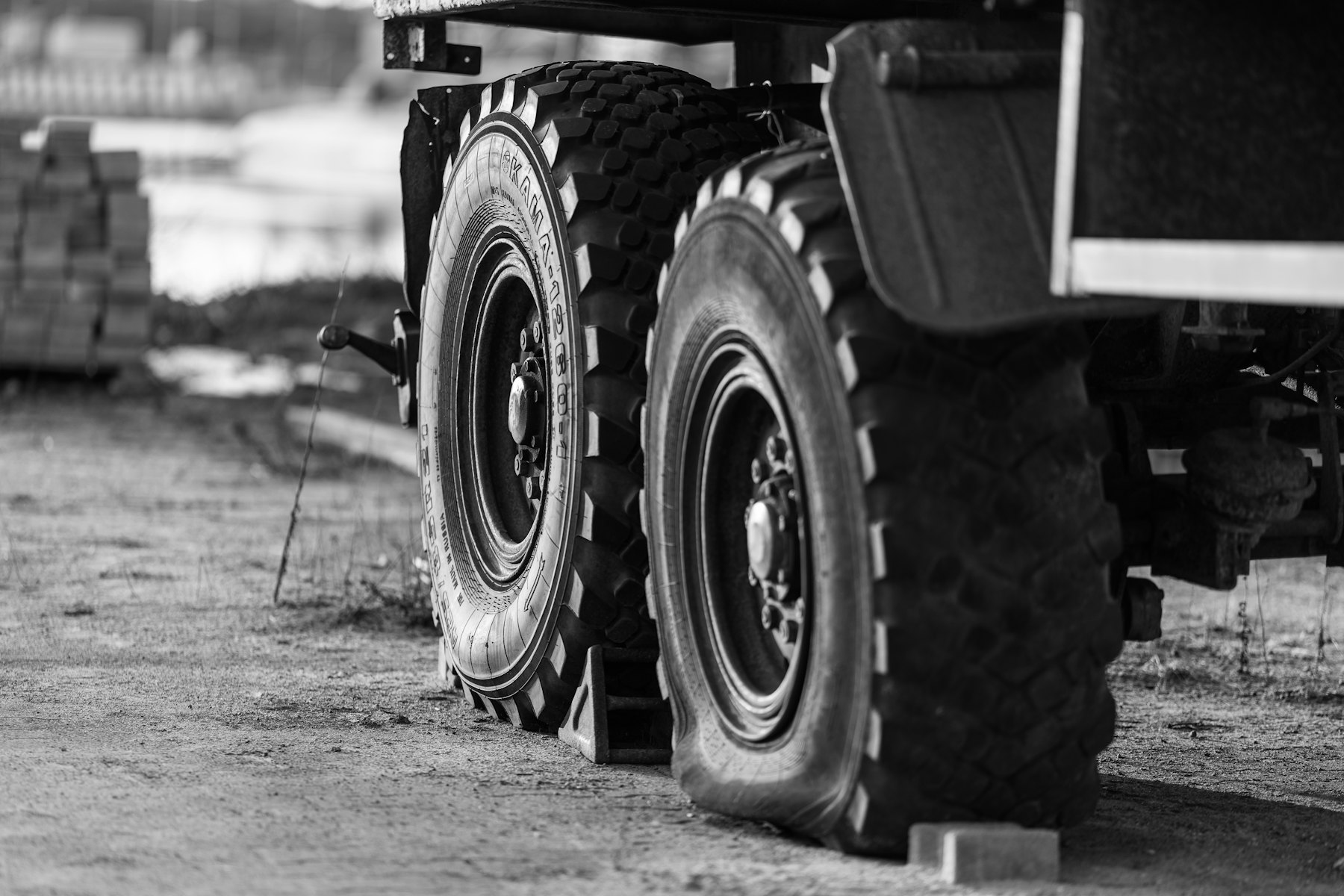 Close view of the paired rear tires of a large dump truck on an unpaved road, in black and white